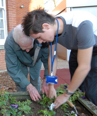 Male NHS staff member tending garden with elderly man